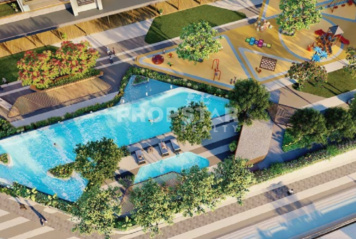 Aerial view of a resort-style residential complex with a large turquoise pool, surrounding greenery, and a colorful playground area.