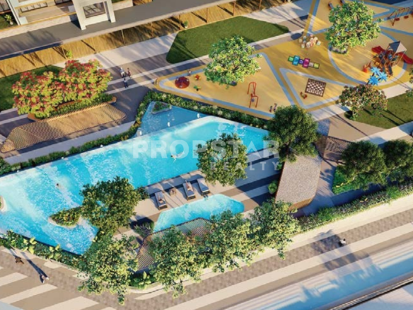Aerial view of a resort-style residential complex with a large turquoise pool, surrounding greenery, and a colorful playground area.