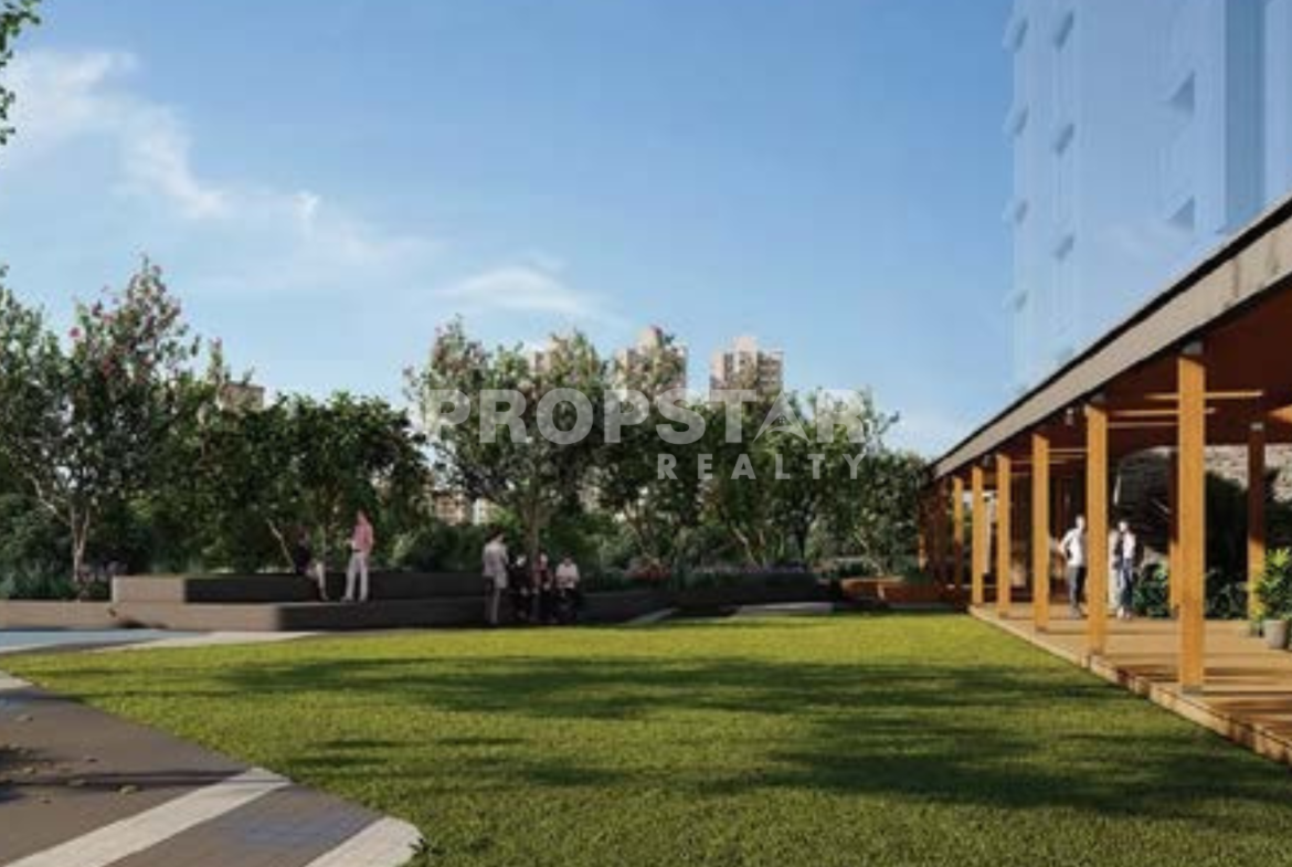 Outdoor community courtyard with manicured lawn, trees, and a wooden pergola building on the right; people strolling and relaxing.