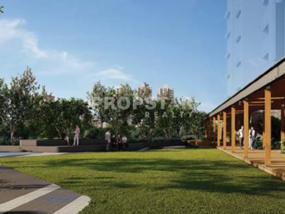 Outdoor community courtyard with manicured lawn, trees, and a wooden pergola building on the right; people strolling and relaxing.